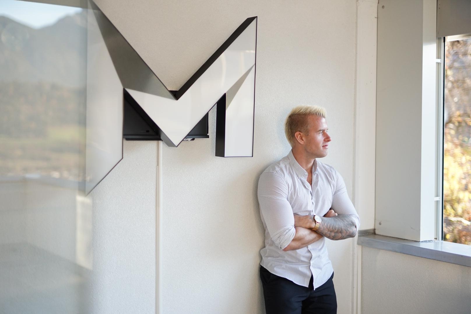 Marco Perner, Portrait stehend, gegen eine Wand gelehnt, neben einem groĂźen PERNER VENTURES Logo.